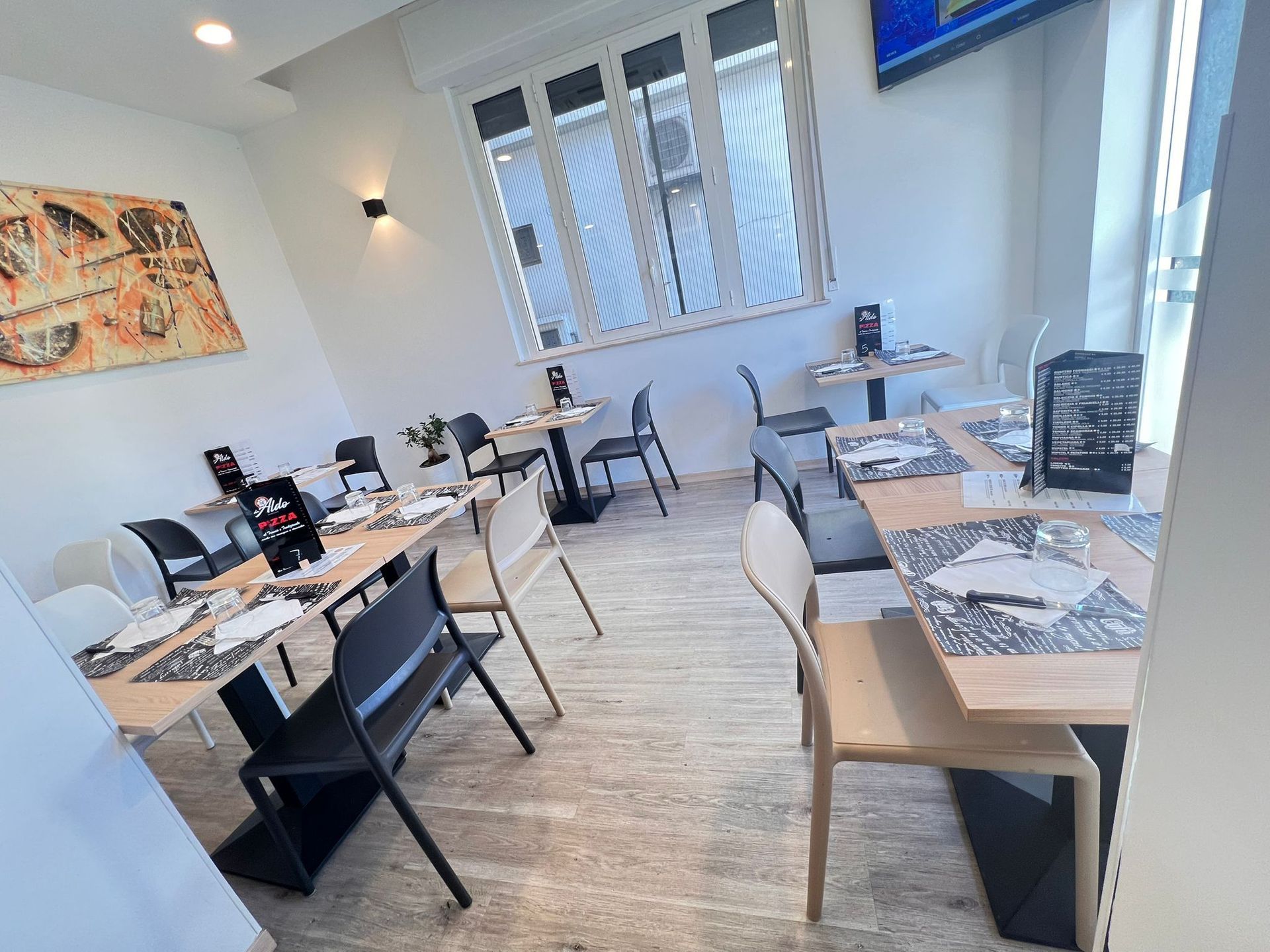 Interno del ristorante con tavoli apparecchiati per mangiare, sedie e finestra con luce naturale.