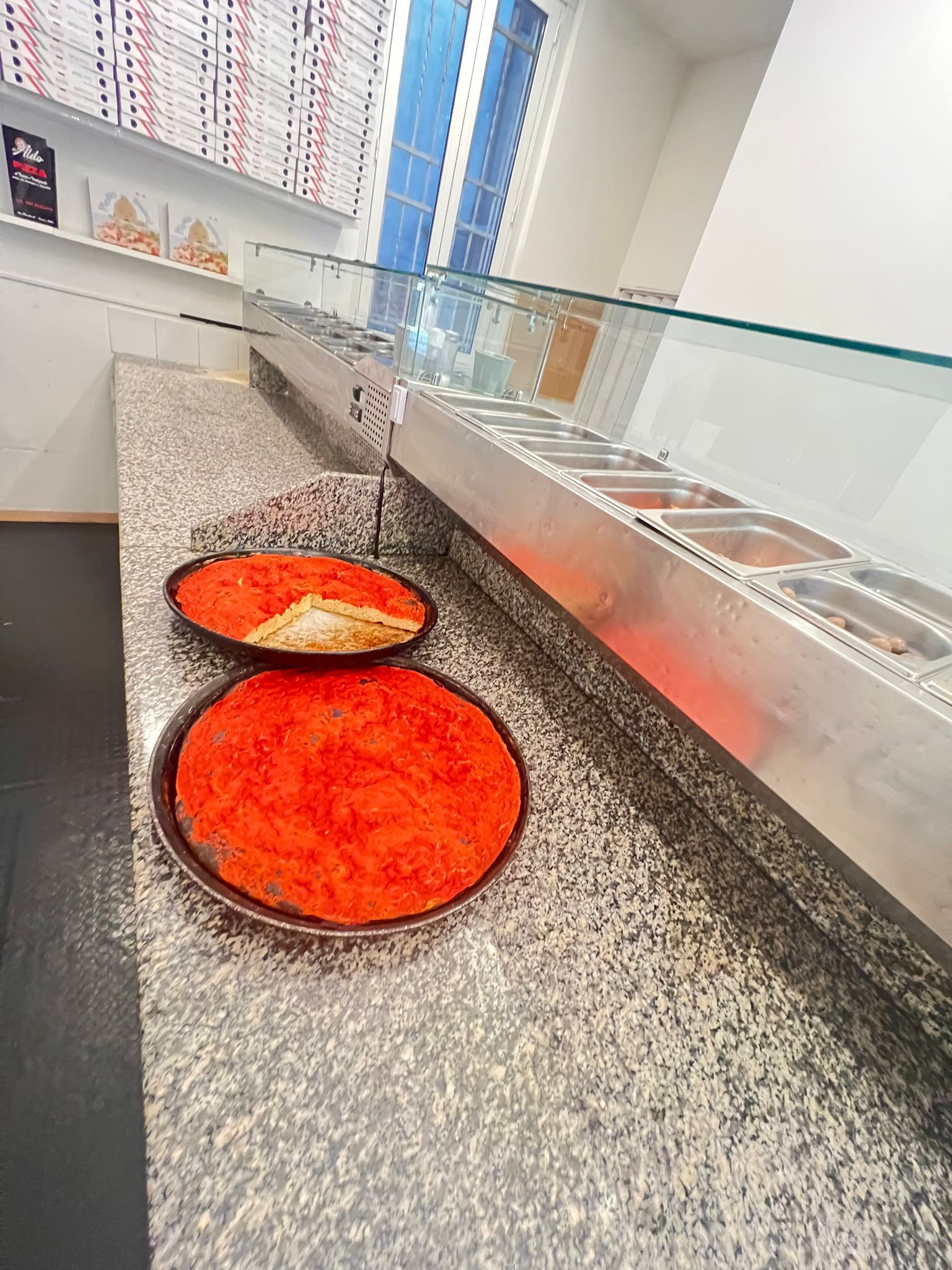 Due vassoi di pasta sfoglia rossa su un bancone punteggiato accanto a una vetrina per alimenti.