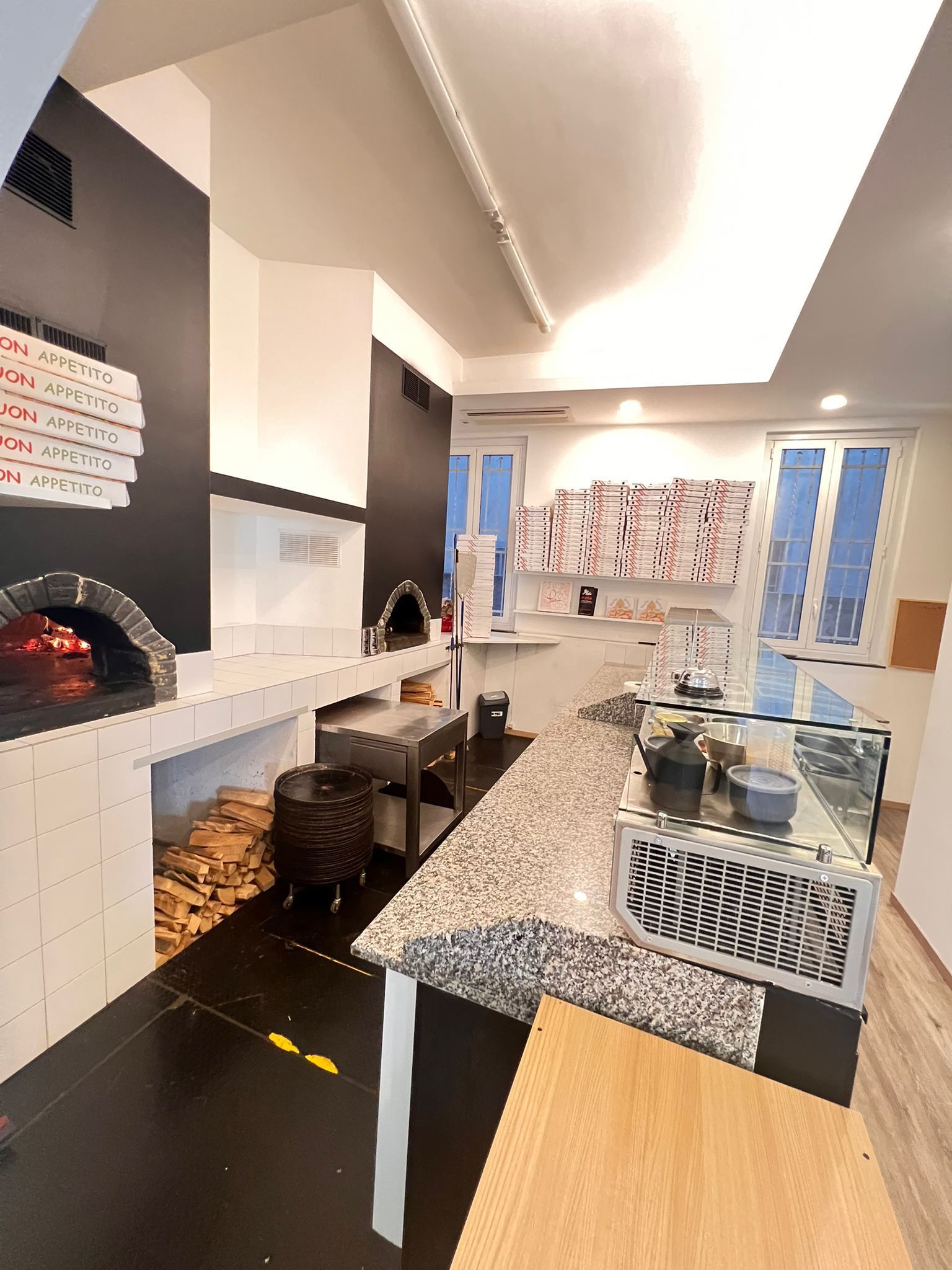 Interno di una pizzeria con forno a legna, area di preparazione del cibo e vetrine.