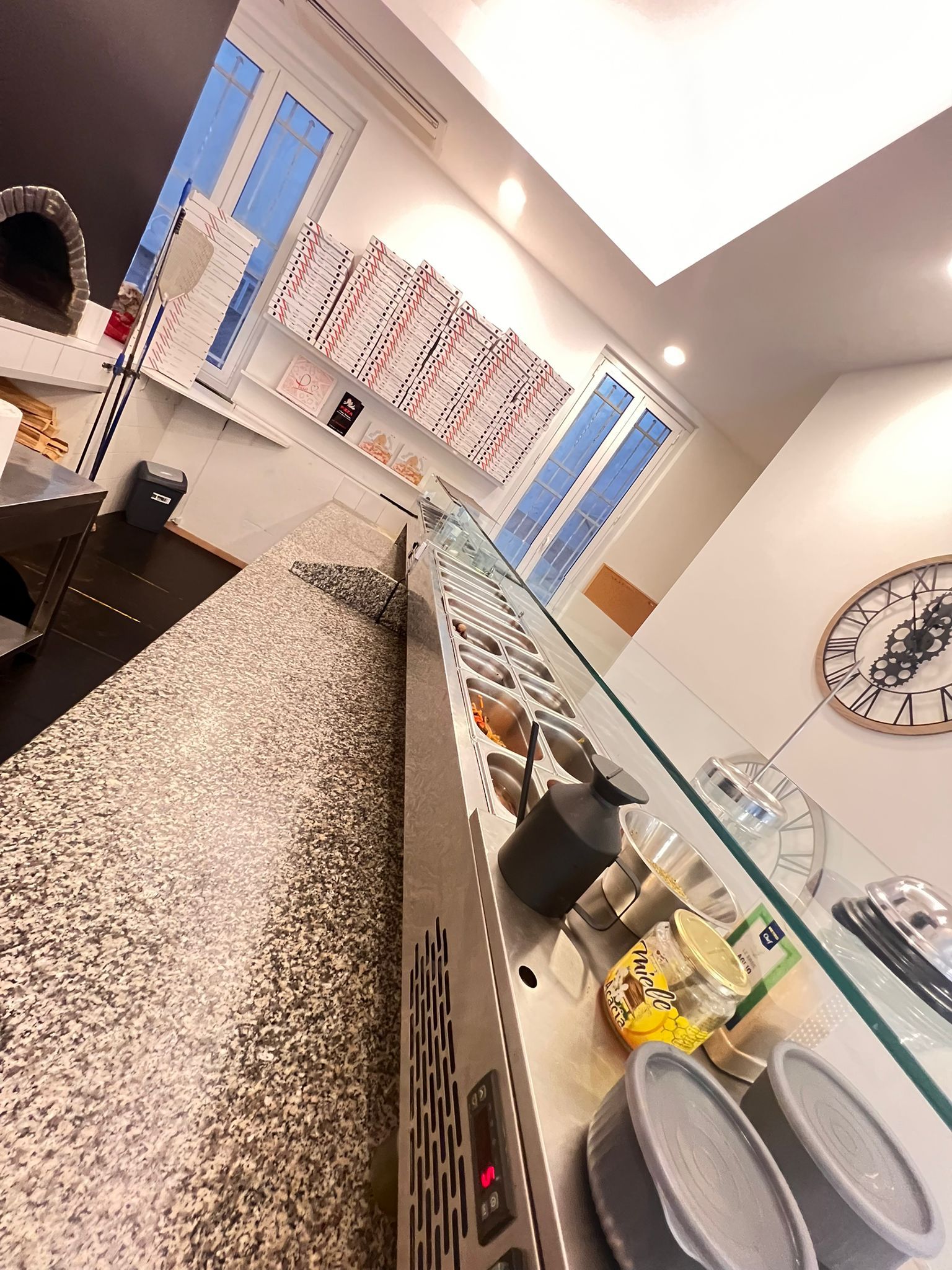 L'interno di un bar con un bancone che espone il cibo. Un orologio e una finestra sono appesi alla parete.
