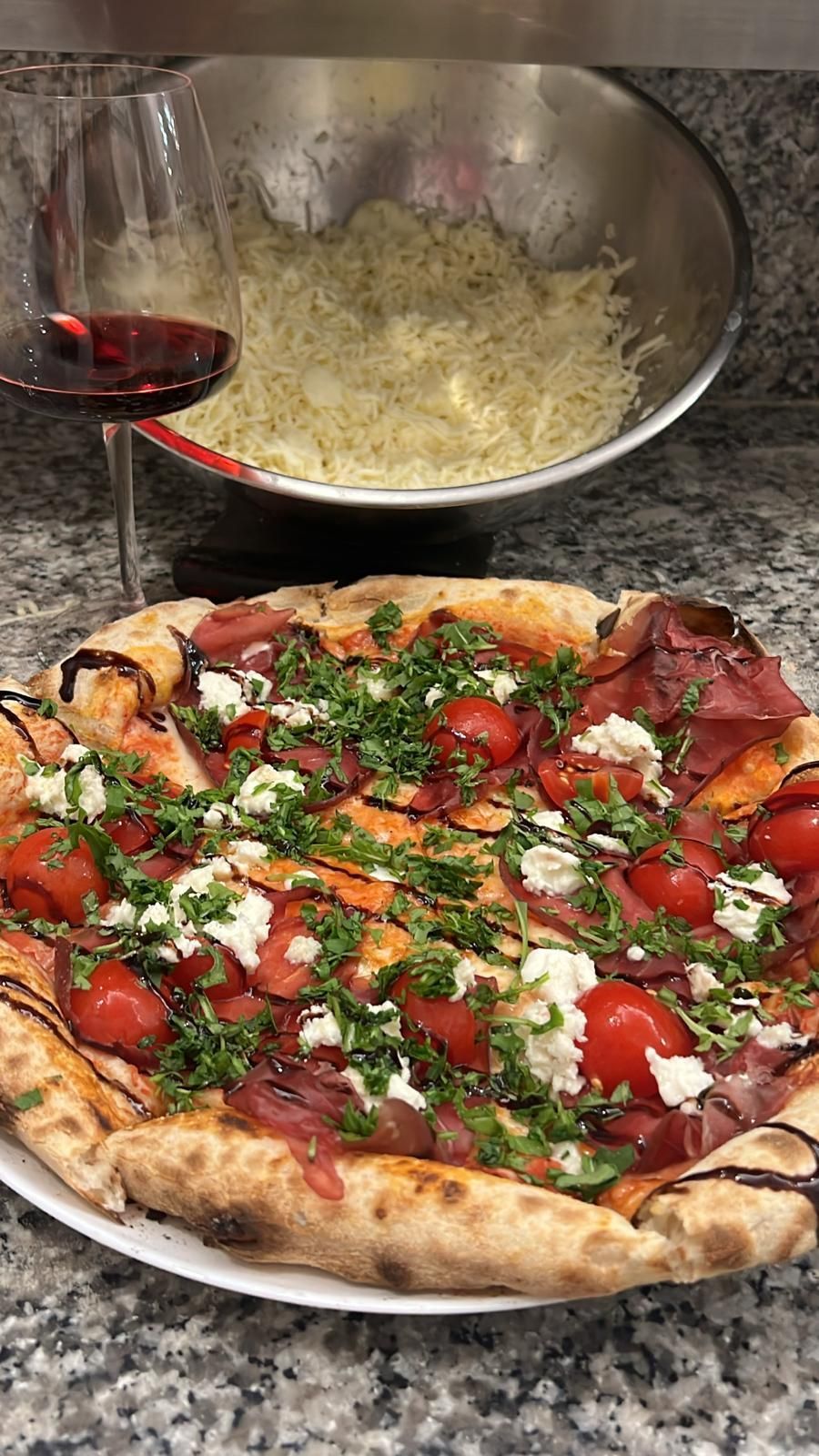 Pizza condita con pomodori, formaggio ed erbe aromatiche, con un bicchiere di vino rosso e una ciotola di formaggio.
