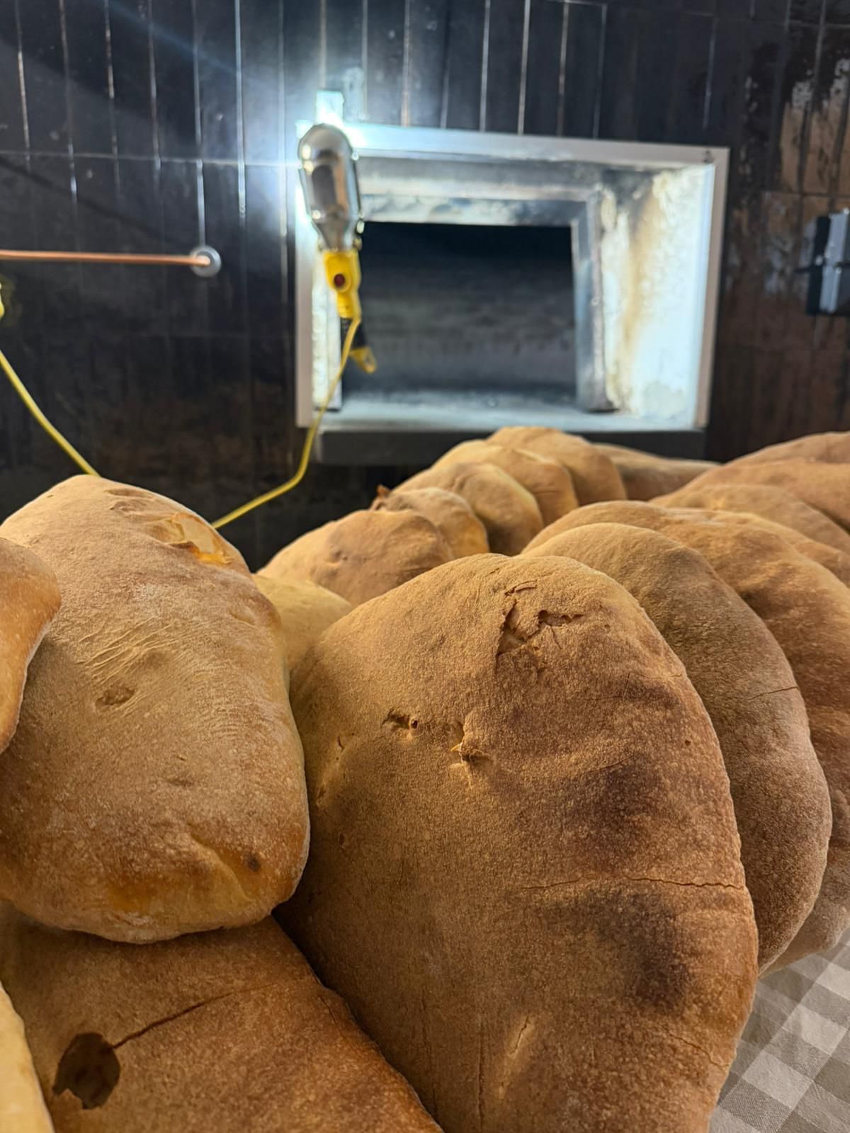 Pane pita appena sfornato, ammucchiato vicino a un forno a legna in una panetteria.