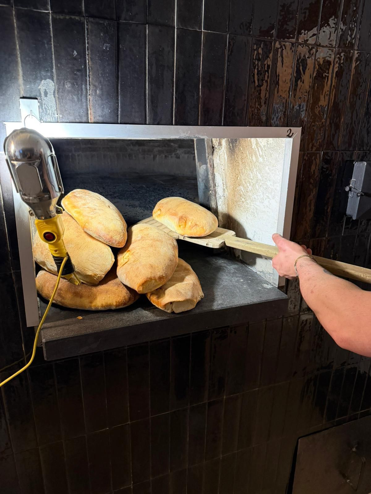 Persona che estrae focacce cotte al forno da un forno commerciale con una pala di legno.