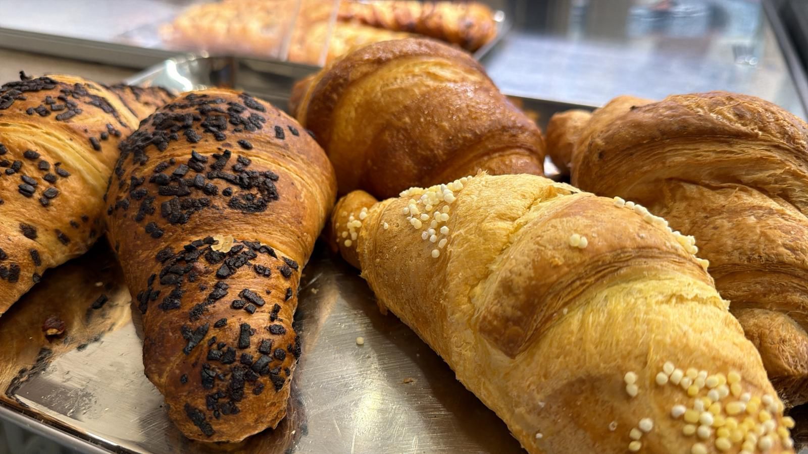 Primo piano di croissant cotti su un vassoio; alcuni sono ricoperti di granella di cioccolato, altri di semi di sesamo.