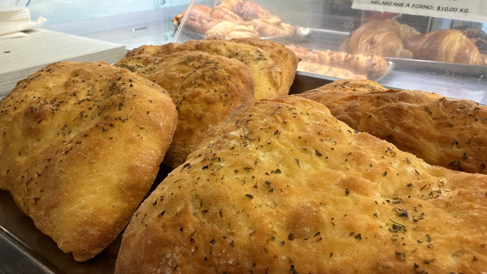 Focaccia alle erbe su un vassoio, croissant sullo sfondo.