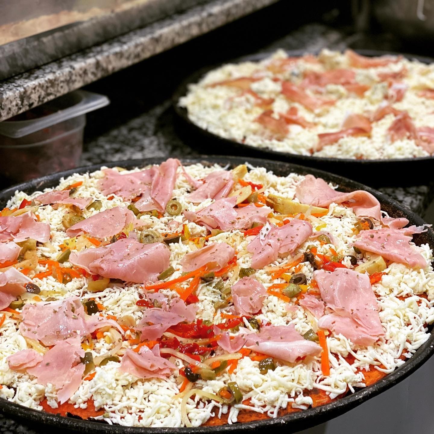 Due pizze condite con prosciutto, formaggio e verdure sul bancone della cucina.