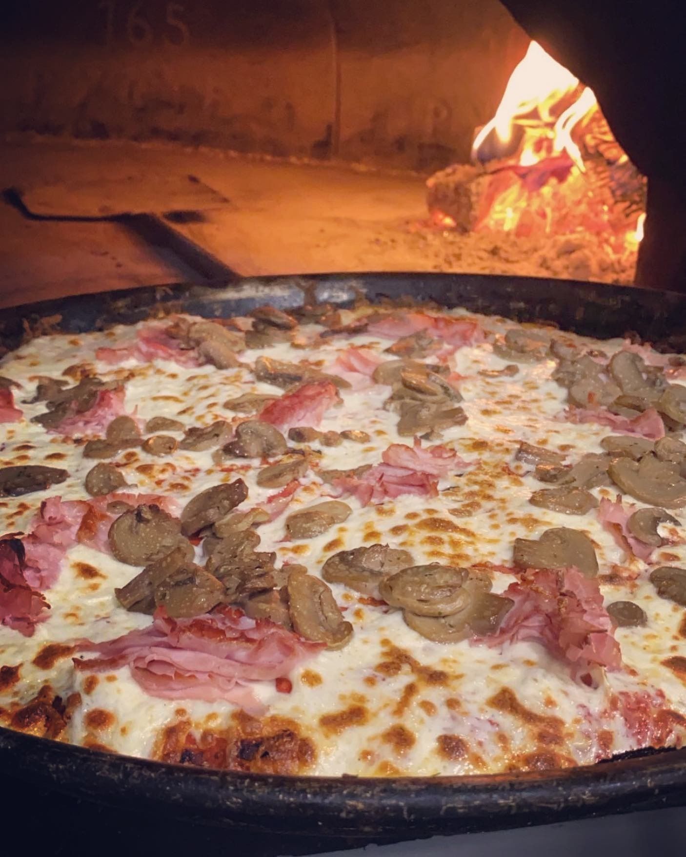 Pizza con prosciutto e funghi cotta nel forno a legna. Fiamme sullo sfondo.