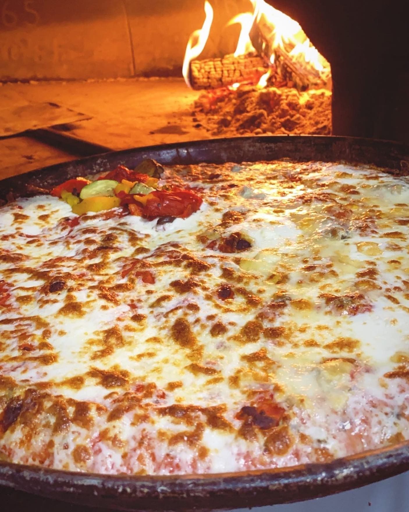 Pizza cotta nel forno a legna con formaggio fuso e verdure arrostite.