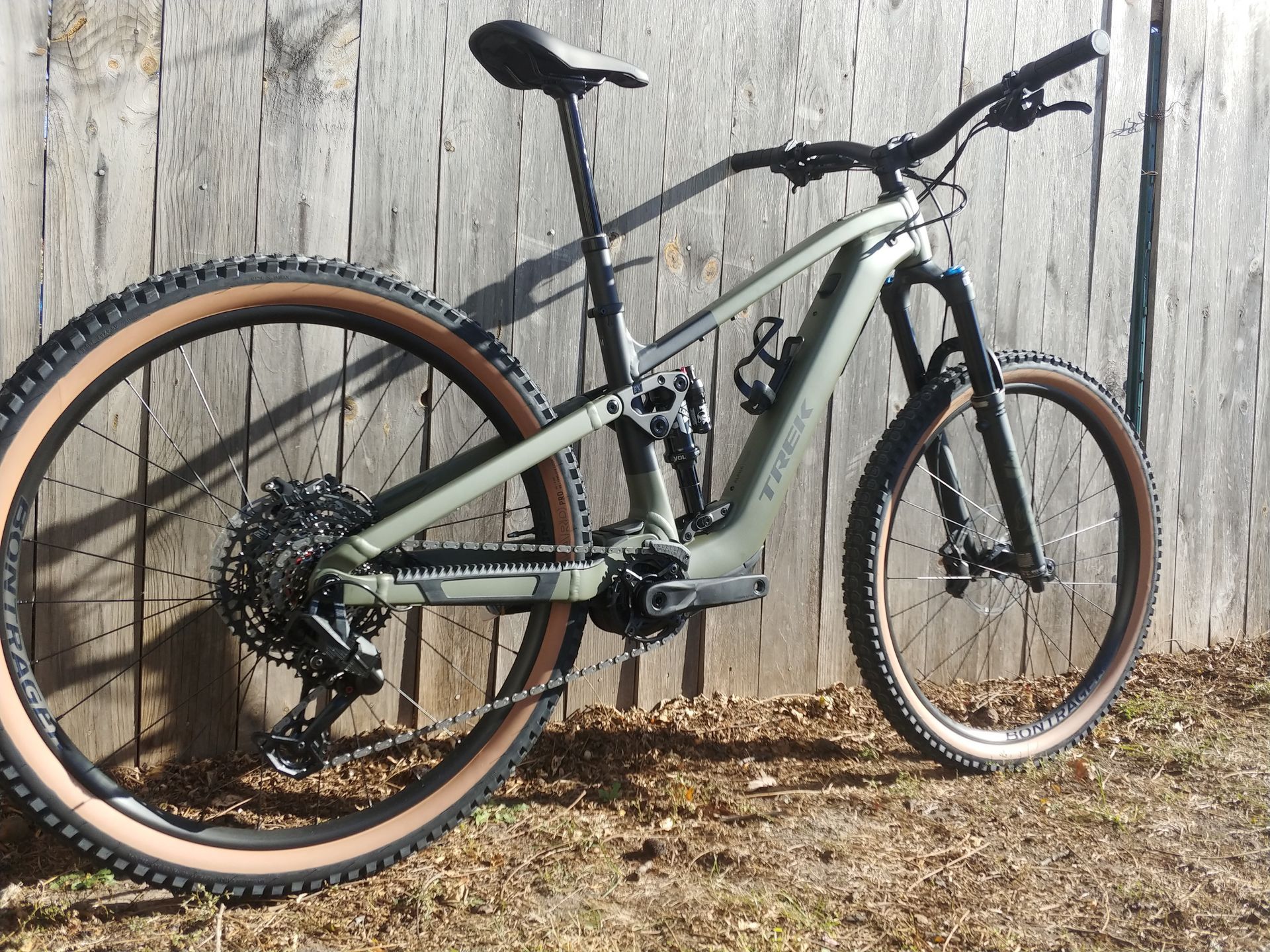 Mountain bike with tan tires leaning against a weathered wooden fence outdoors.