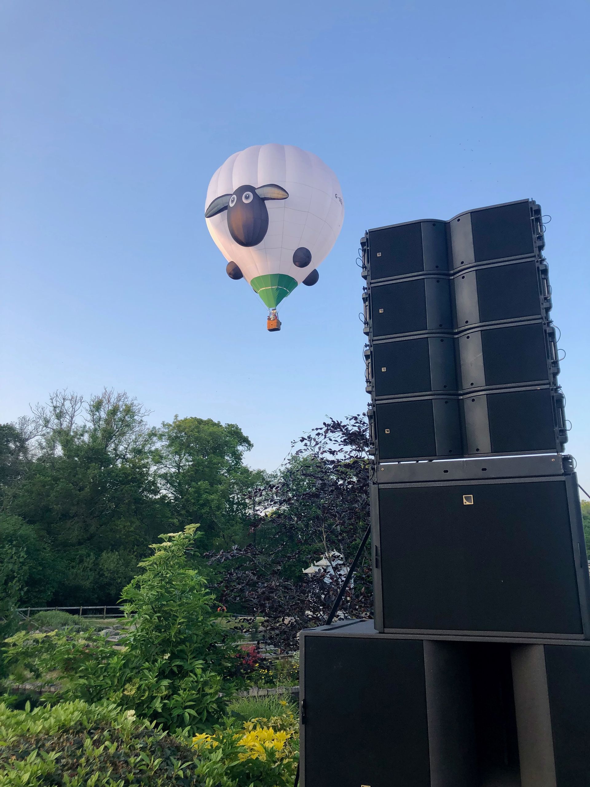 A hot air balloon with a sheep on it is flying over a stack of speakers