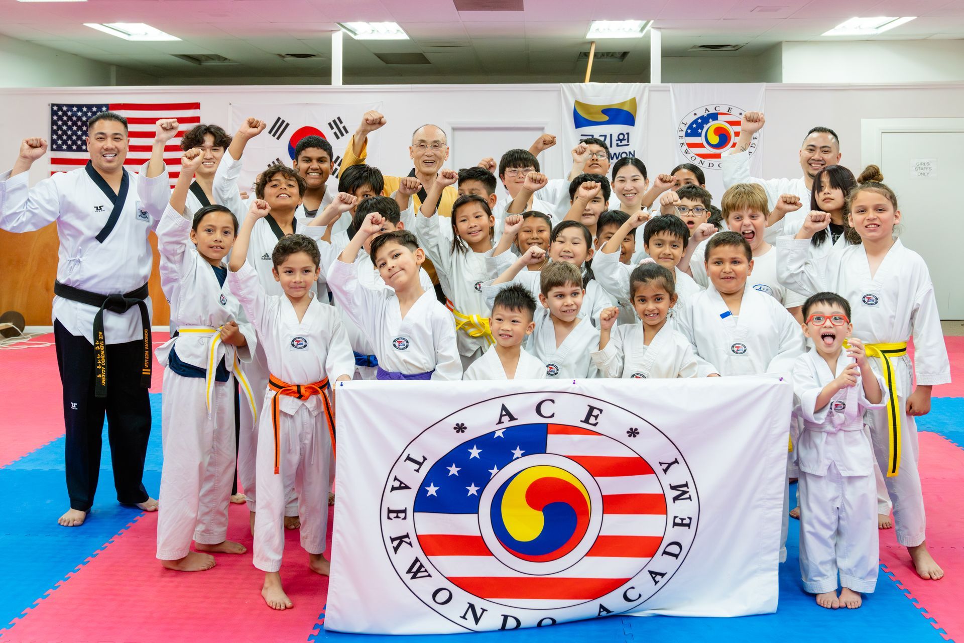 Two people in martial arts uniforms stand before American and South Korean flags; one holds a gold trophy.