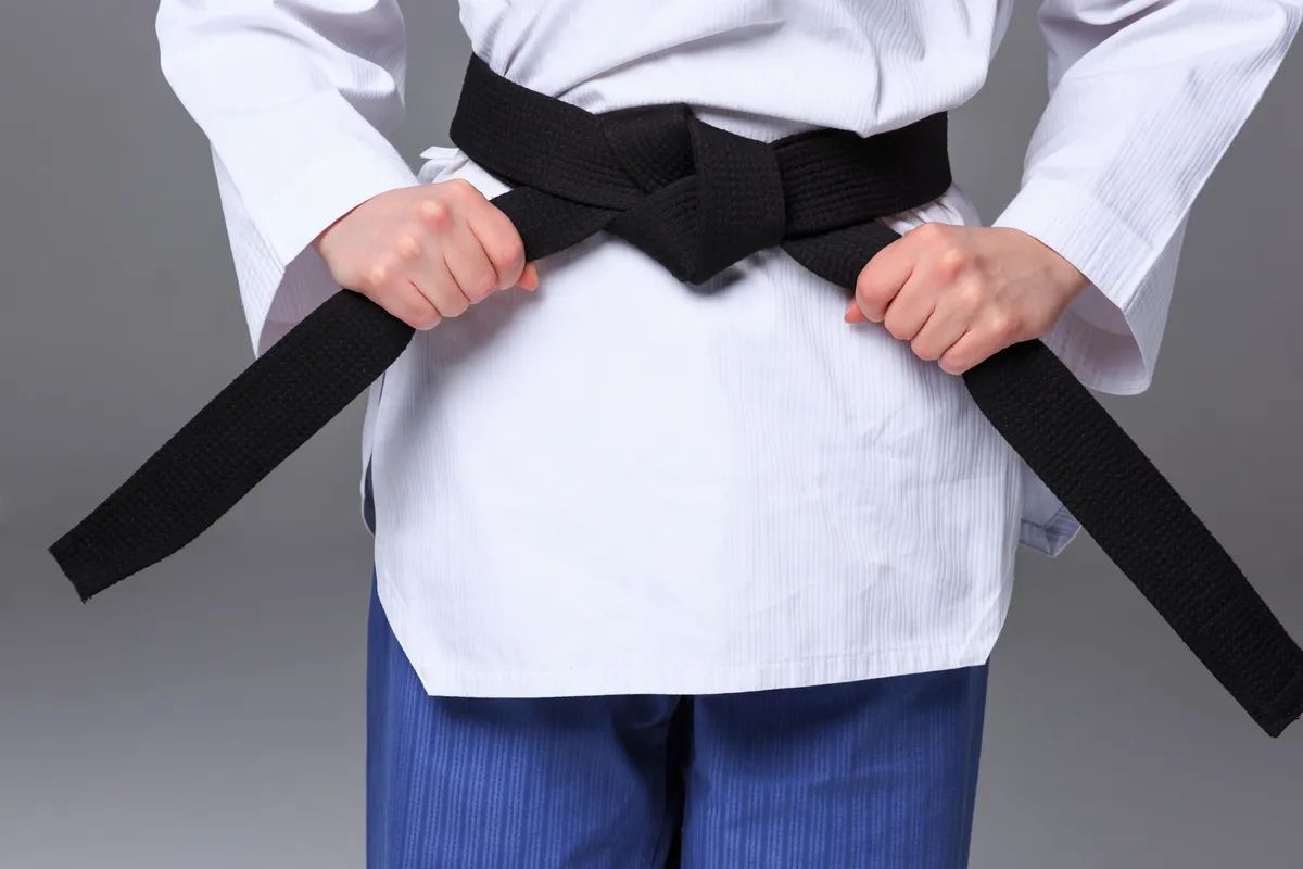 A person in a white martial arts uniform cinching a black belt around their waist.