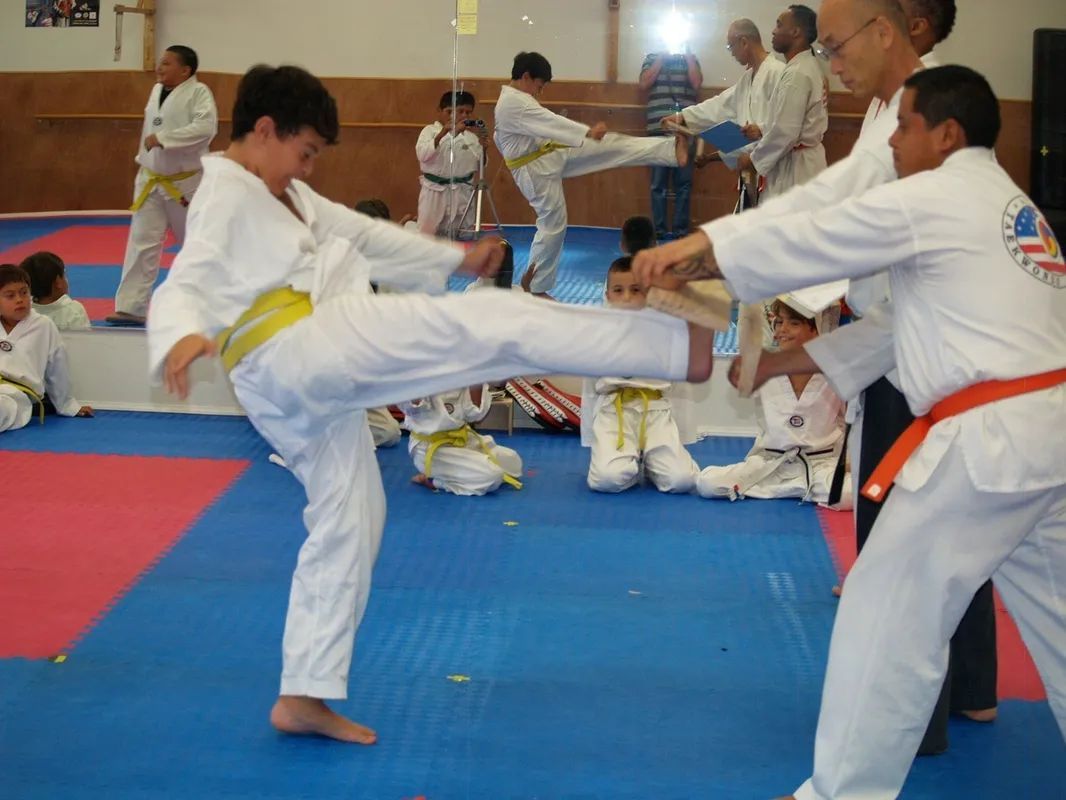 Two people in martial arts uniforms stand before American and South Korean flags; one holds a gold trophy.