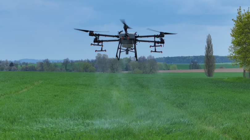 Drone spraying a field with white liquid, outdoors.