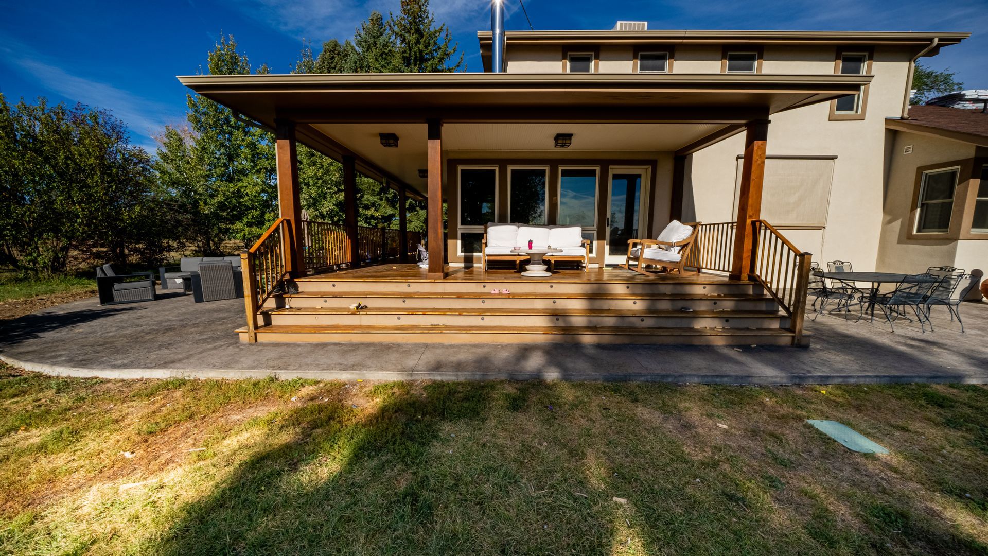 Modern house with a covered wooden porch, lounge chairs, and a grassy yard in front