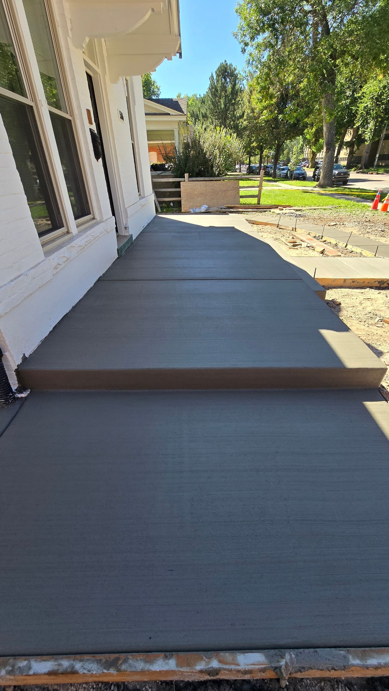 Freshly poured concrete patio beside a house, leading to a landscaped yard with trees and stepping stones.