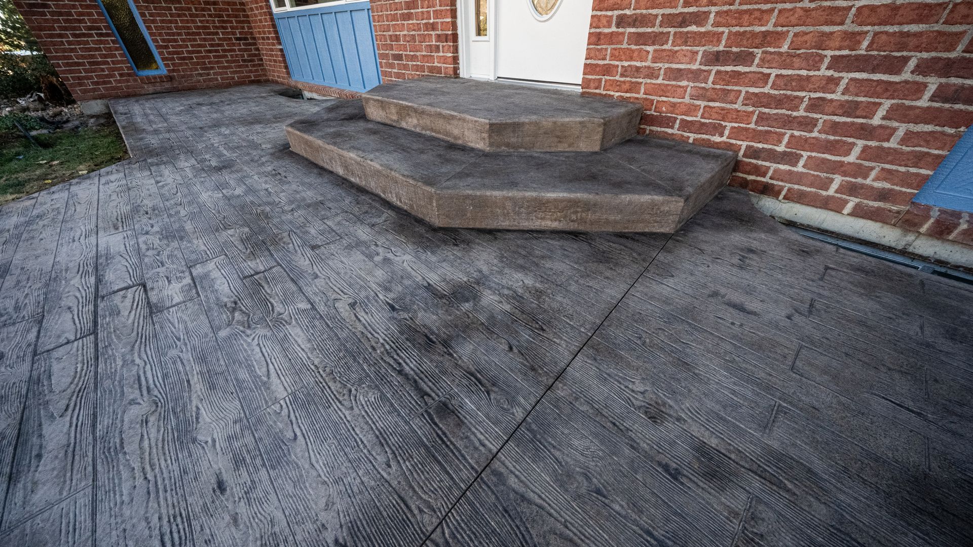 Concrete patio with a small brick stoop and steps leading to a white door beside a red brick wall.