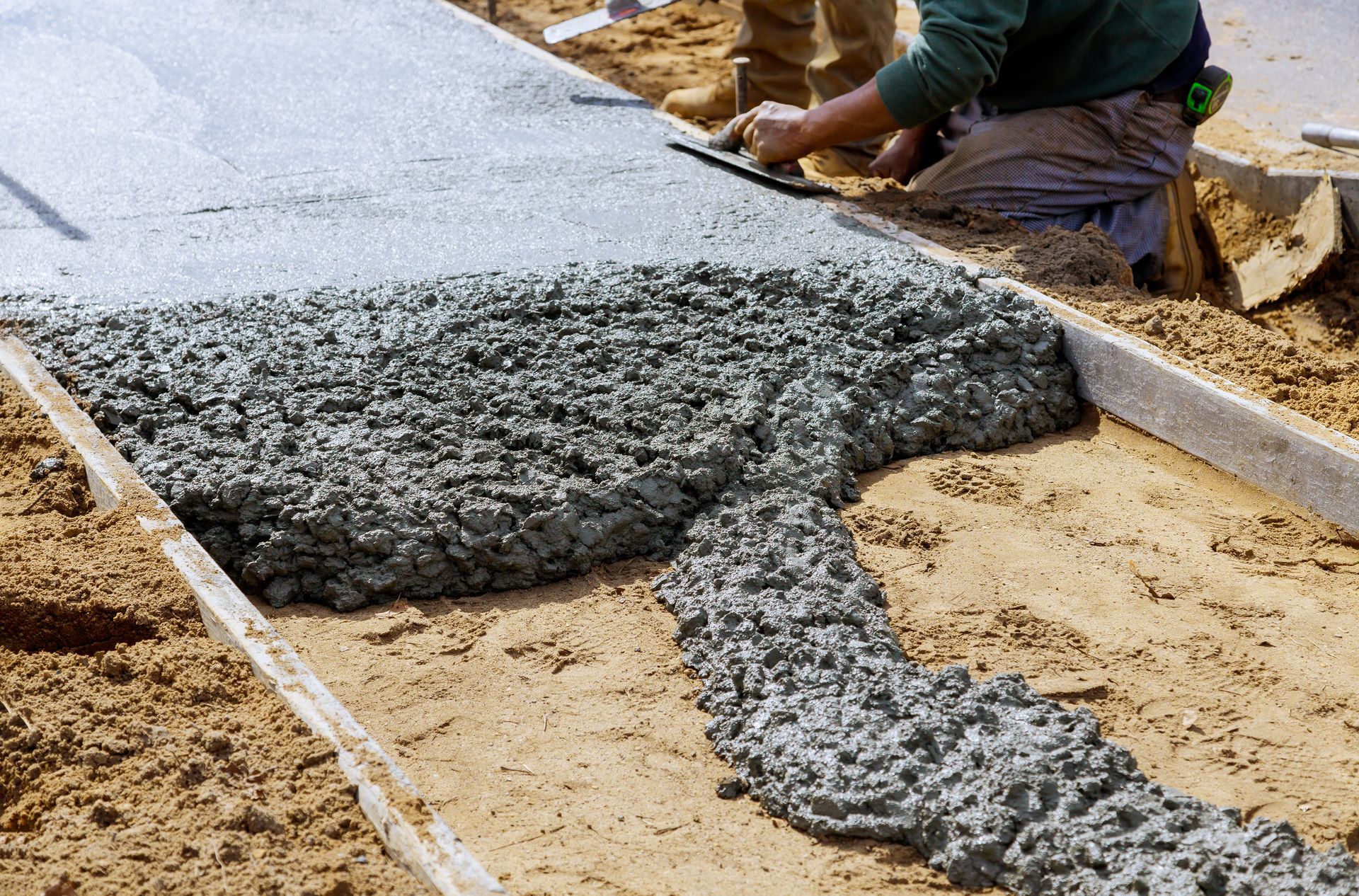 Worker pouring wet concrete into a sand form at a construction site