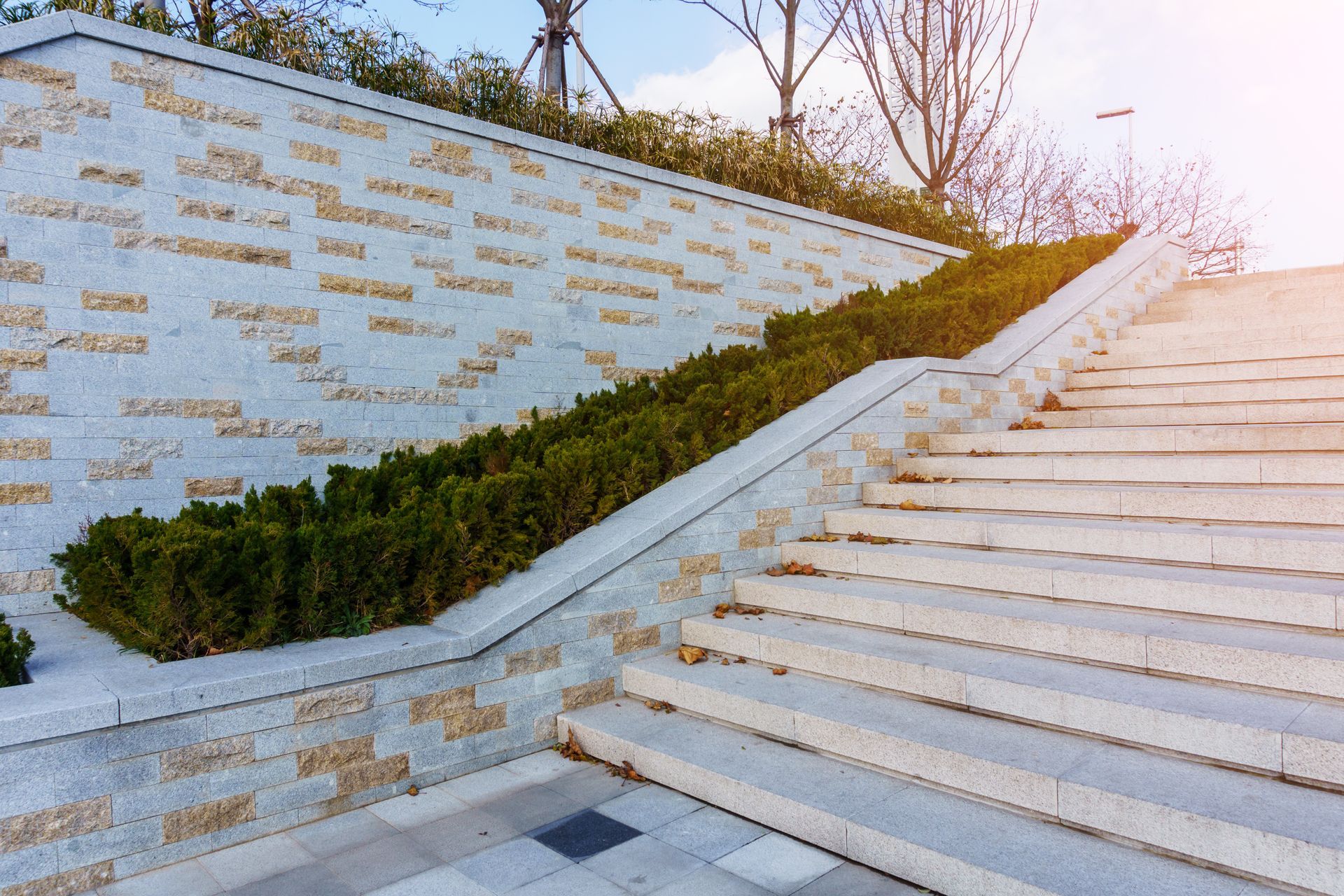 Stone staircase beside a sloped wall with gold lettering and trimmed greenery at sunset