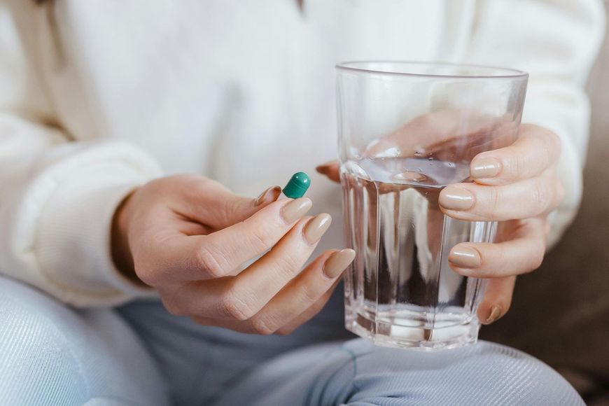 A woman is taking a pill and drinking a glass of water.
