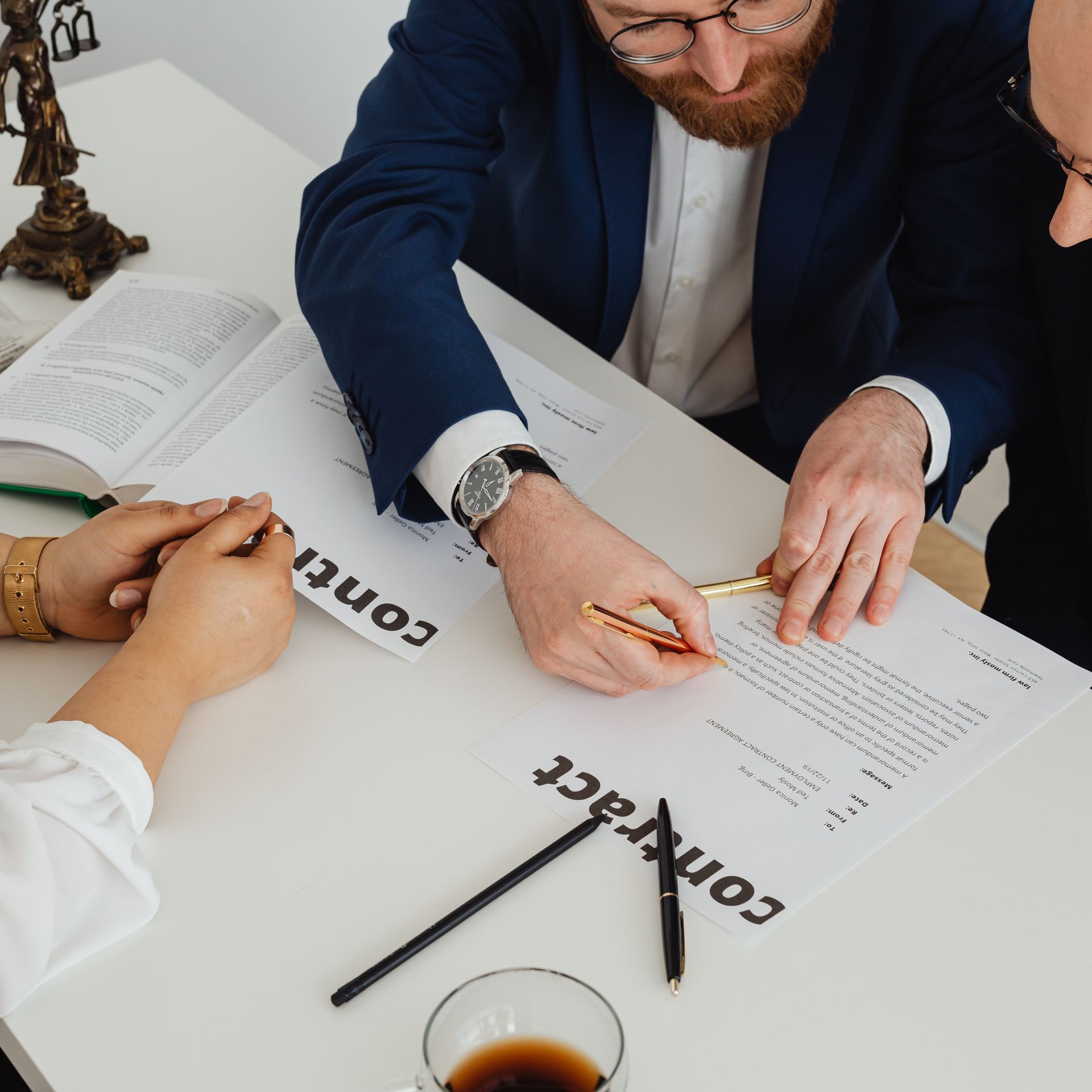 People reviewing and signing a contract at a white table with pens, coffee, and documents.