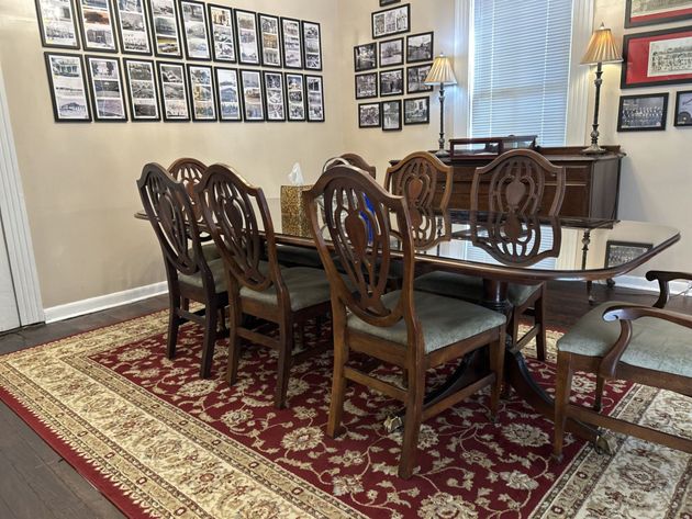 Formal dining room with dark wood table, patterned rug, framed wall photos, and piano by a window