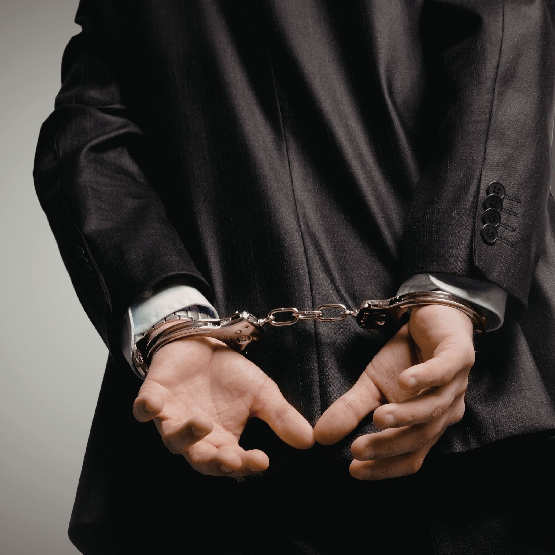 Hands cuffed behind back, wearing a dark suit and chain restraints.