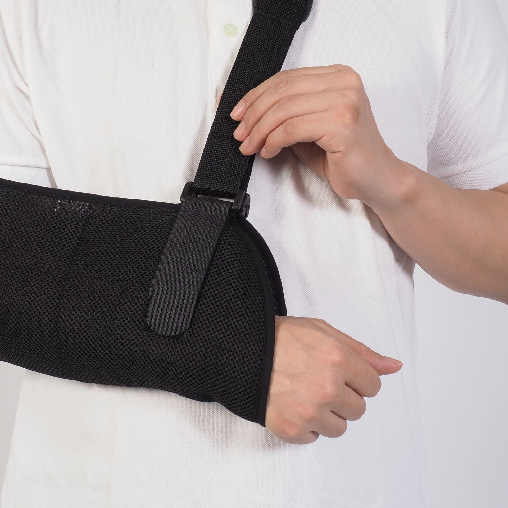 Person wearing a black arm sling and wrist support over a white shirt