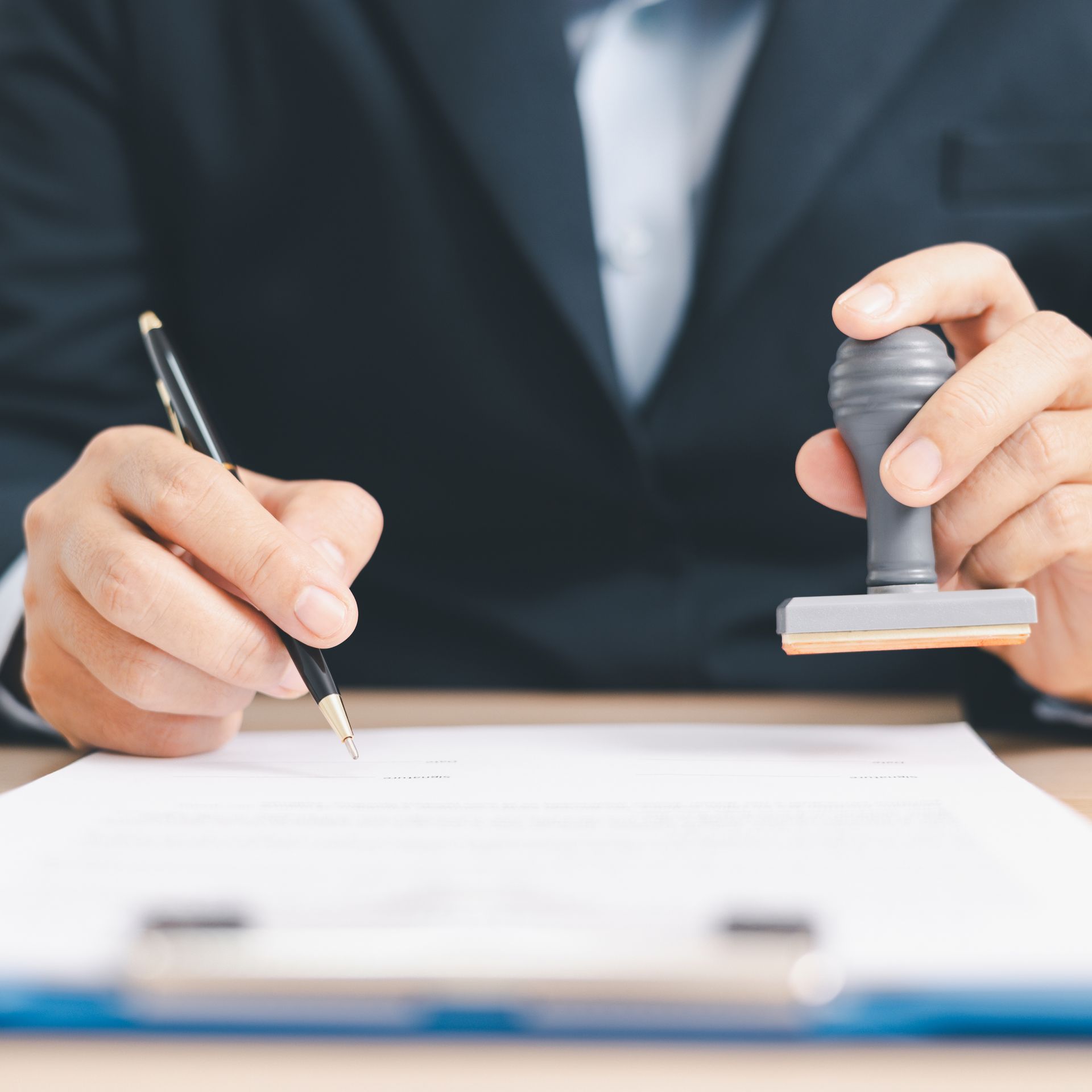 Close-up of hands signing a document with a pen and stamping it on a desk