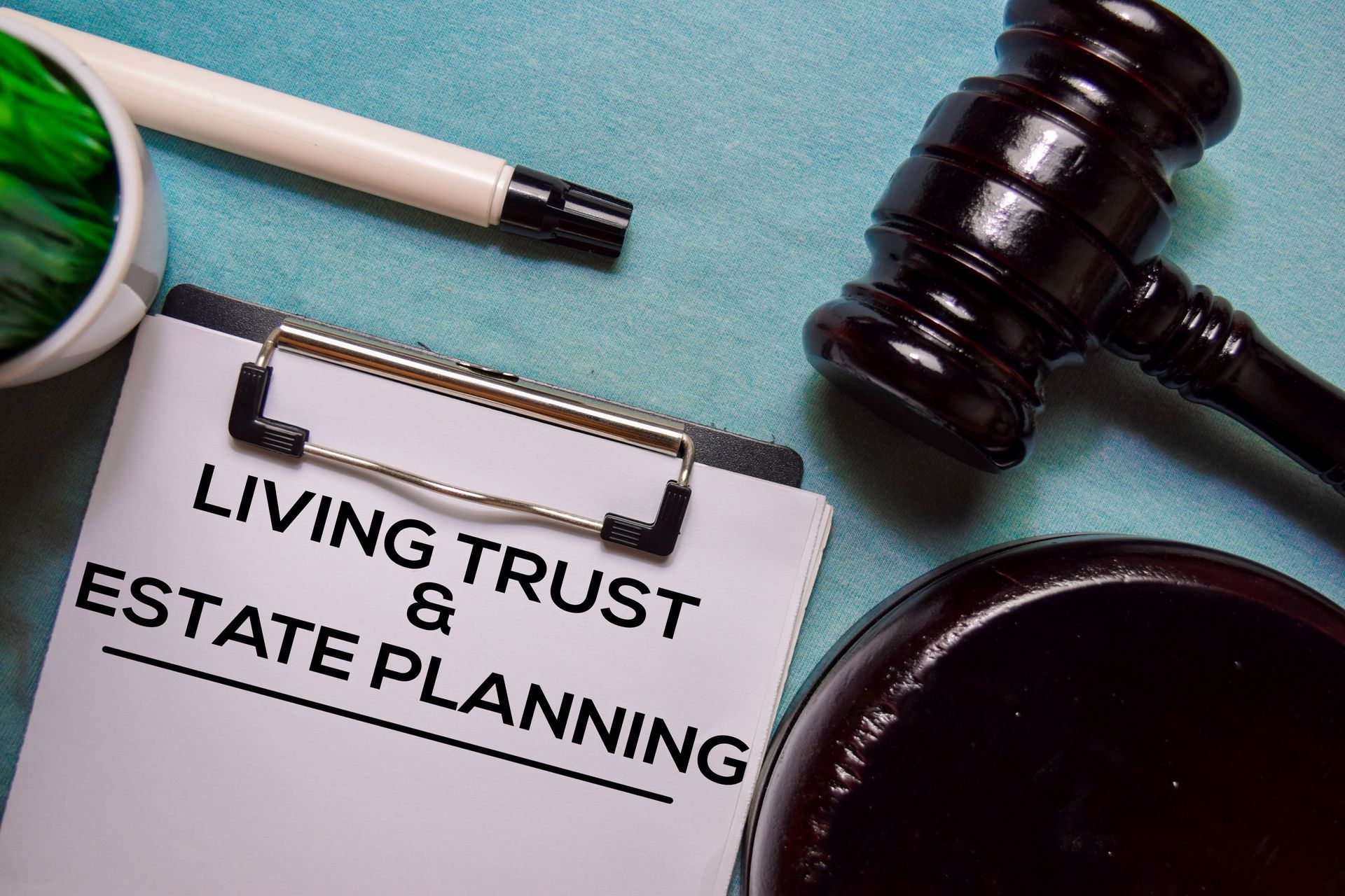 Clipboard with “Living Trust & Estate Planning” beside pen, gavel, and glasses on desk