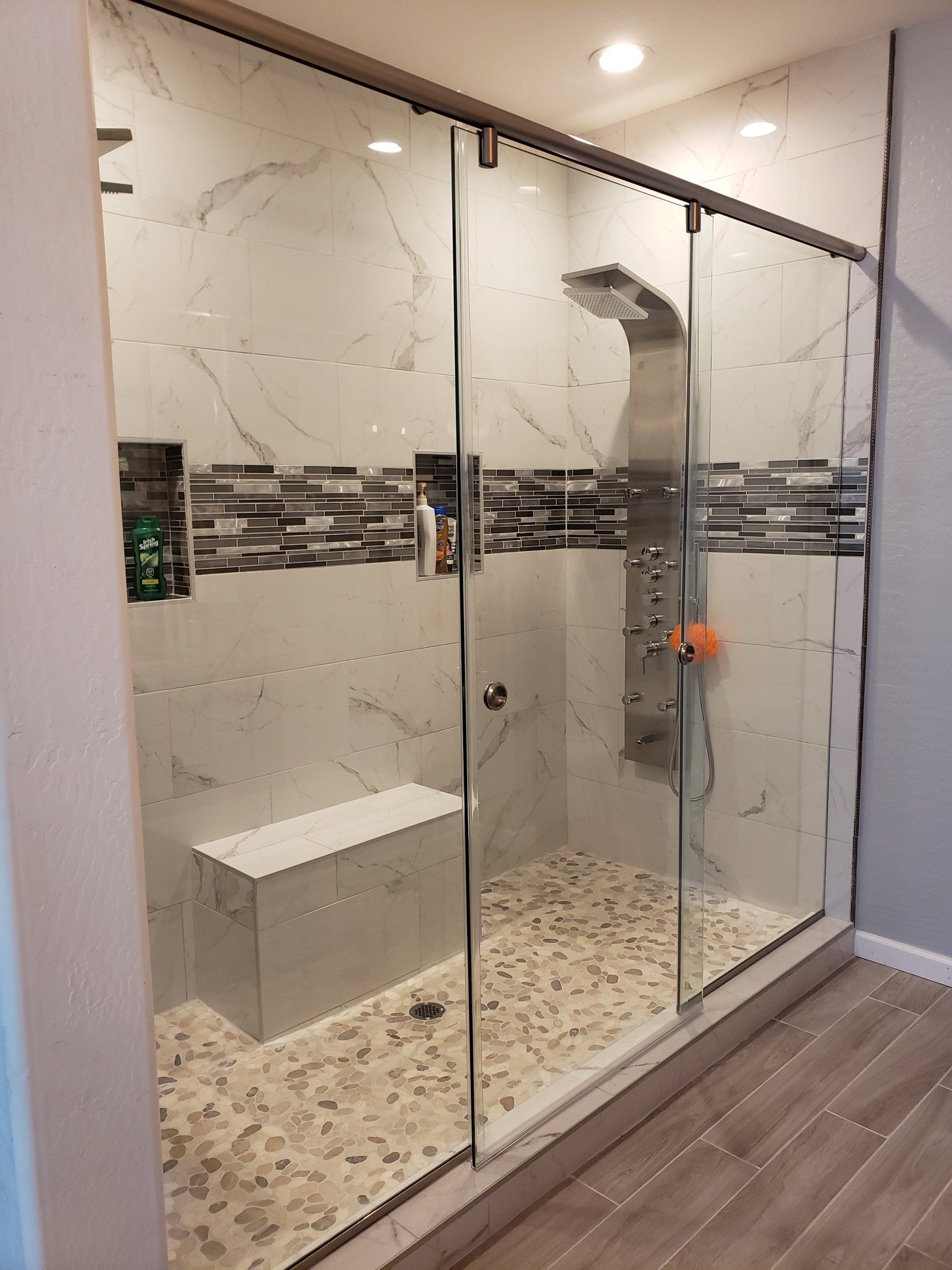 A bathroom with a walk in shower with sliding glass doors and a bench.