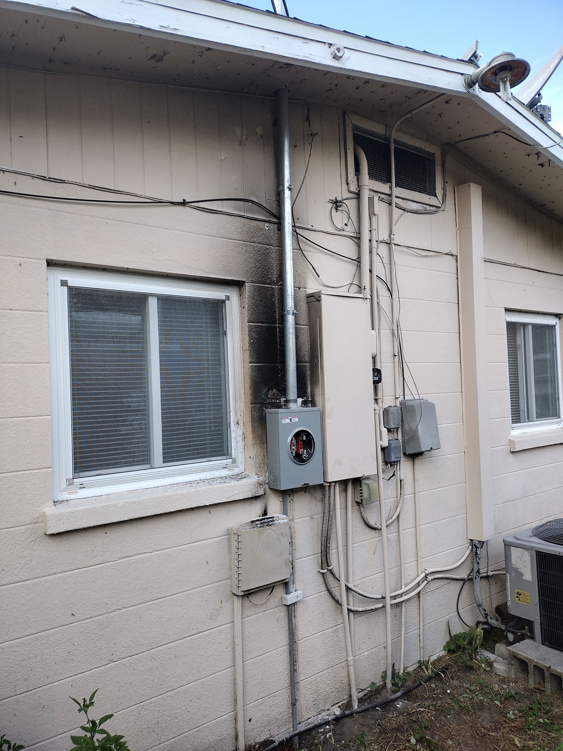Exterior of a house with charred siding, electrical boxes, and conduit. A window is to the left.