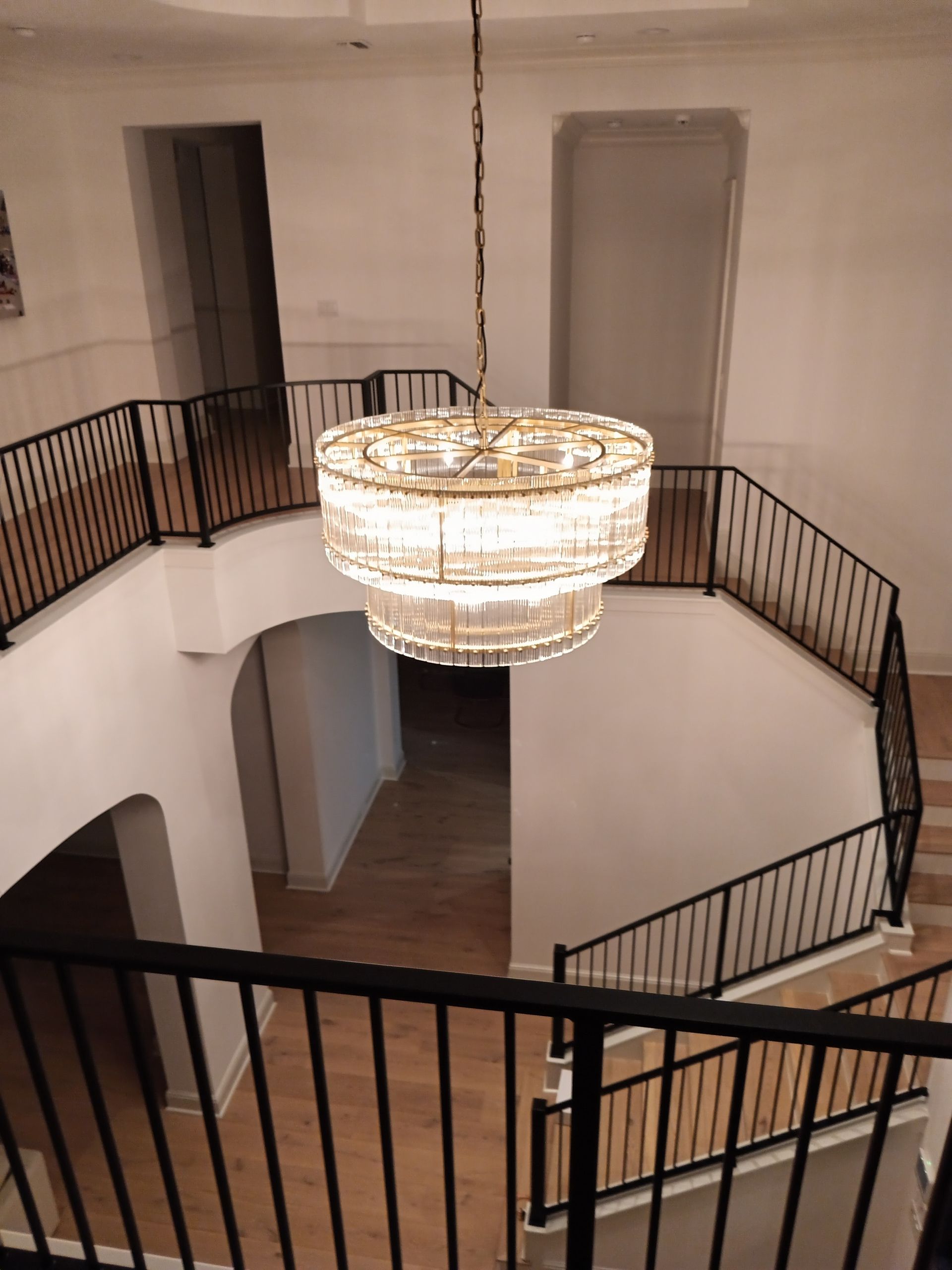 Grand white staircase with black railings, chandelier hangs in the center.