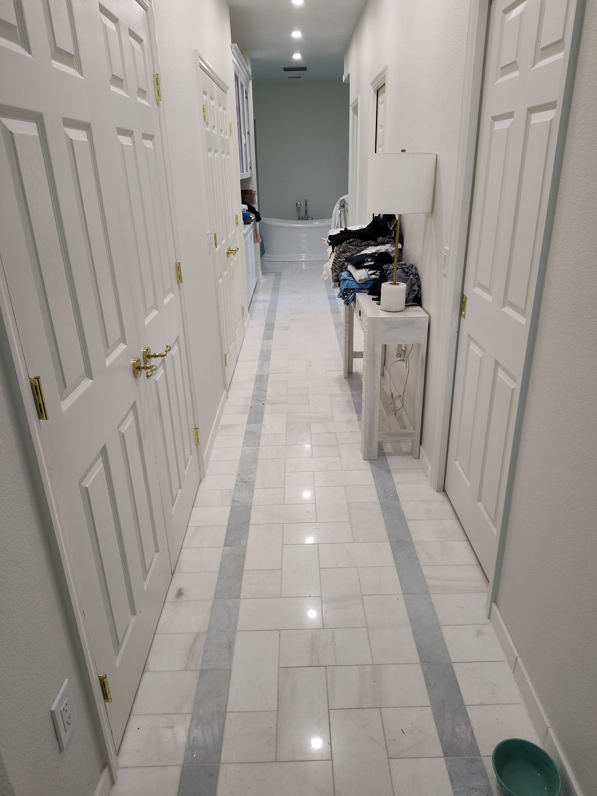 Long hallway with white doors, marble floors, and a bathroom at the end.