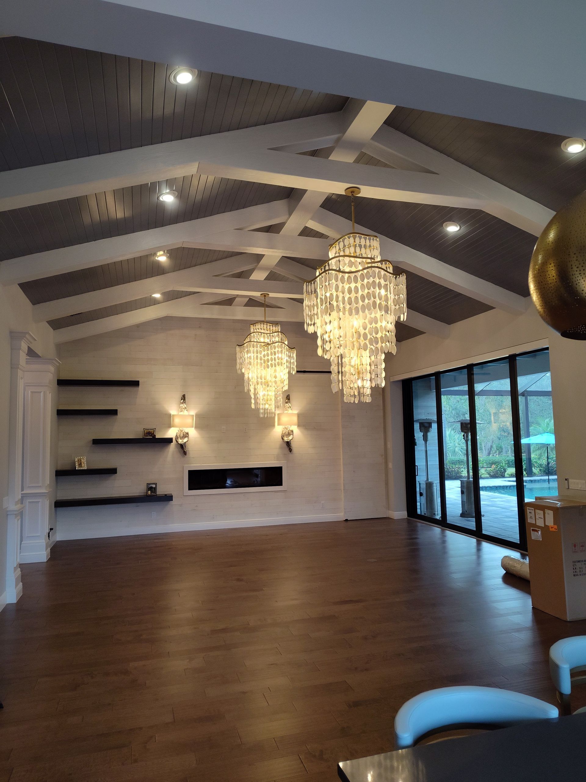 Spacious room with wood floors, vaulted ceiling, chandeliers, fireplace, and sliding glass doors.