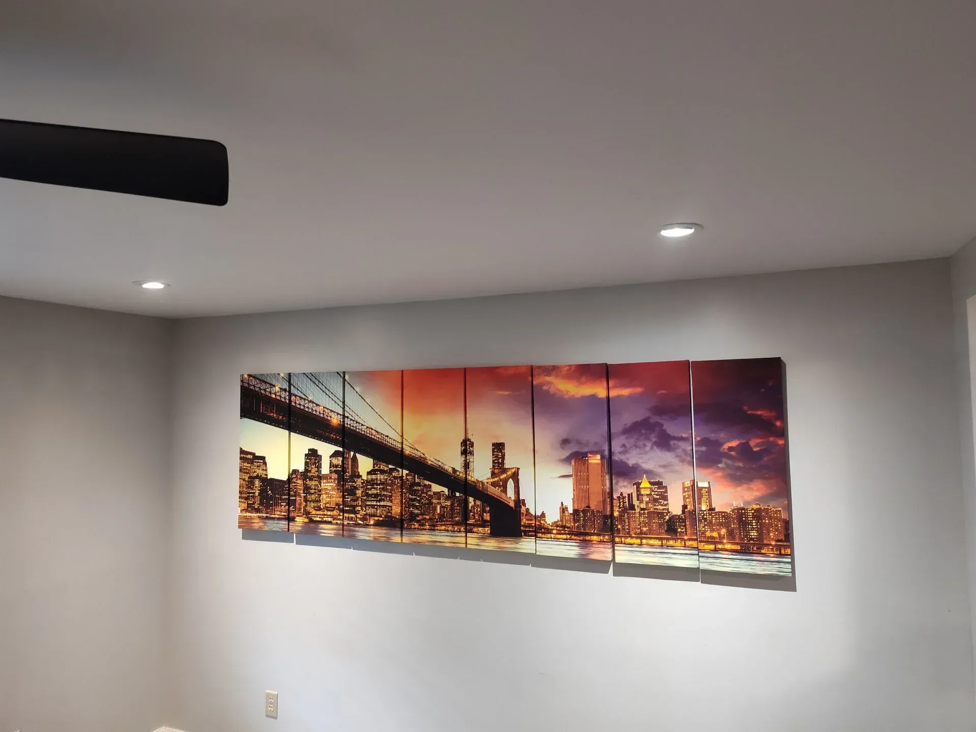 Panoramic city skyline artwork on a white wall; lit by recessed lights.