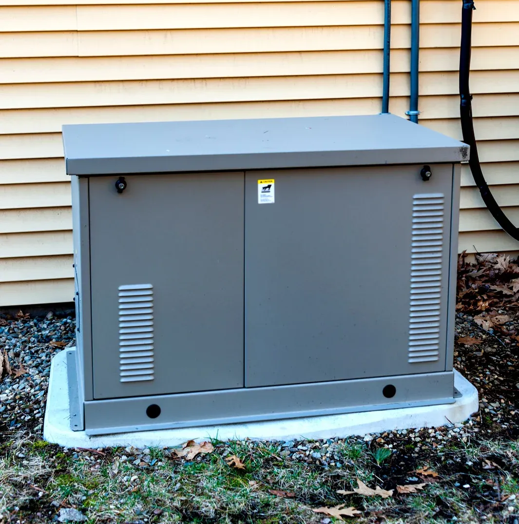 Gray generator enclosure mounted on a concrete pad next to a building.