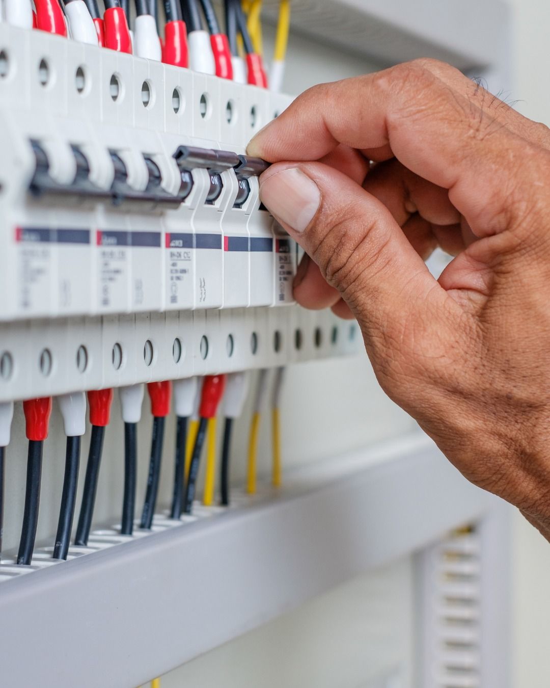 Hand flipping a circuit breaker in an electrical panel, with red and white wires.