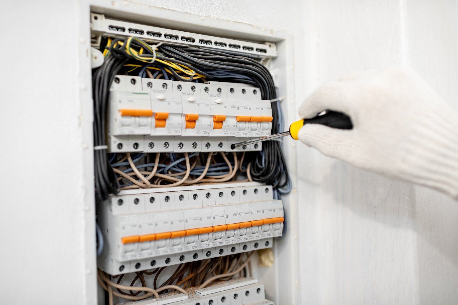 Person in white glove uses screwdriver on electrical panel.