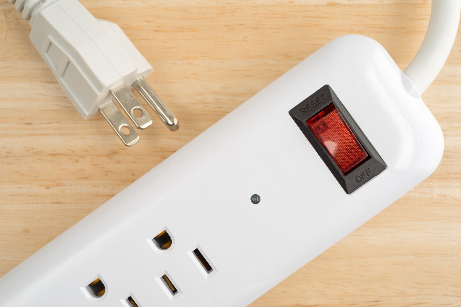 White power strip with a red on/off switch and a plug, on a wooden surface.