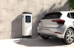 An electric car charging station connected to a silver hatchback parked in a driveway.