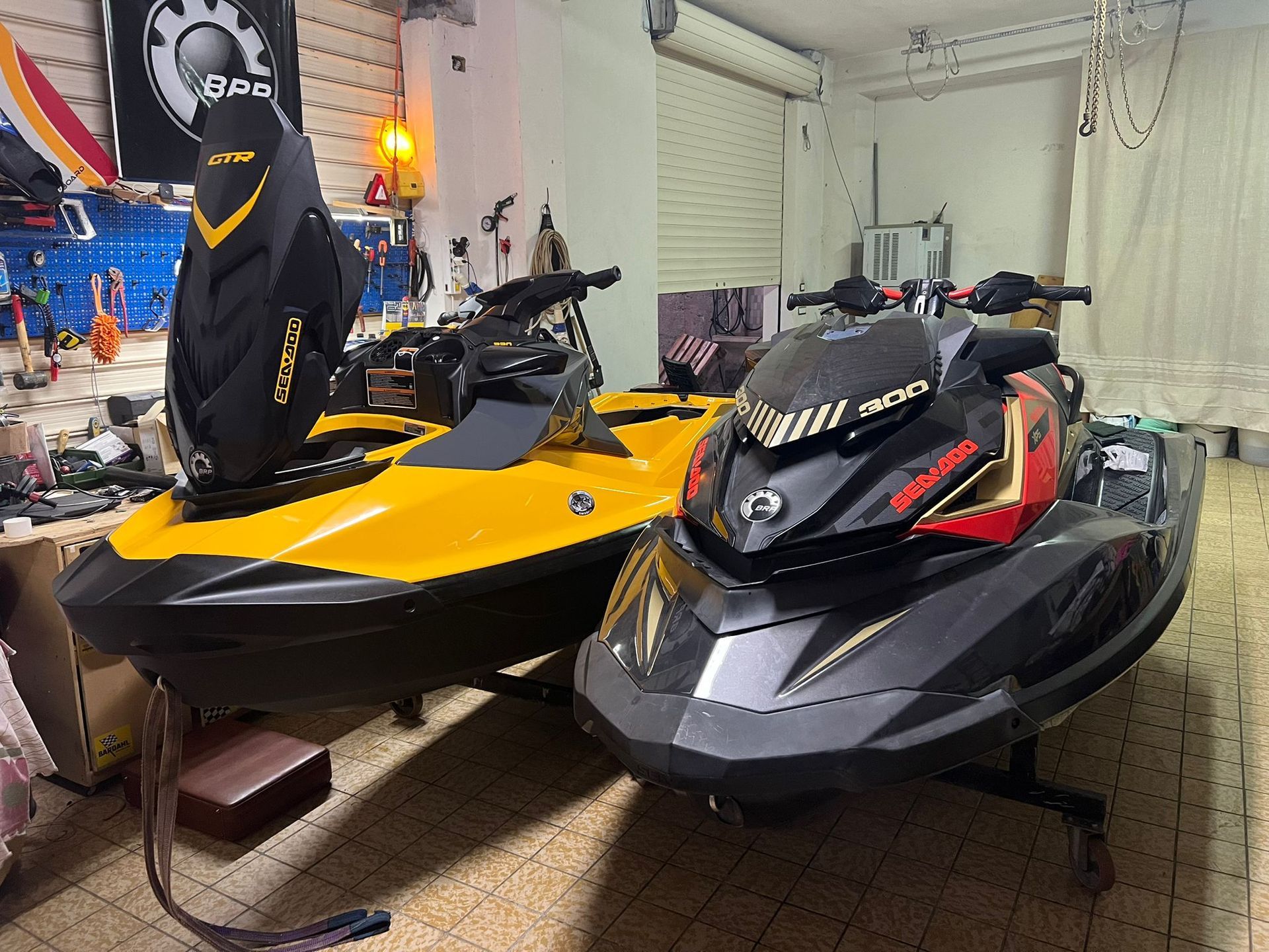 Two jet skis are parked next to each other in a garage.