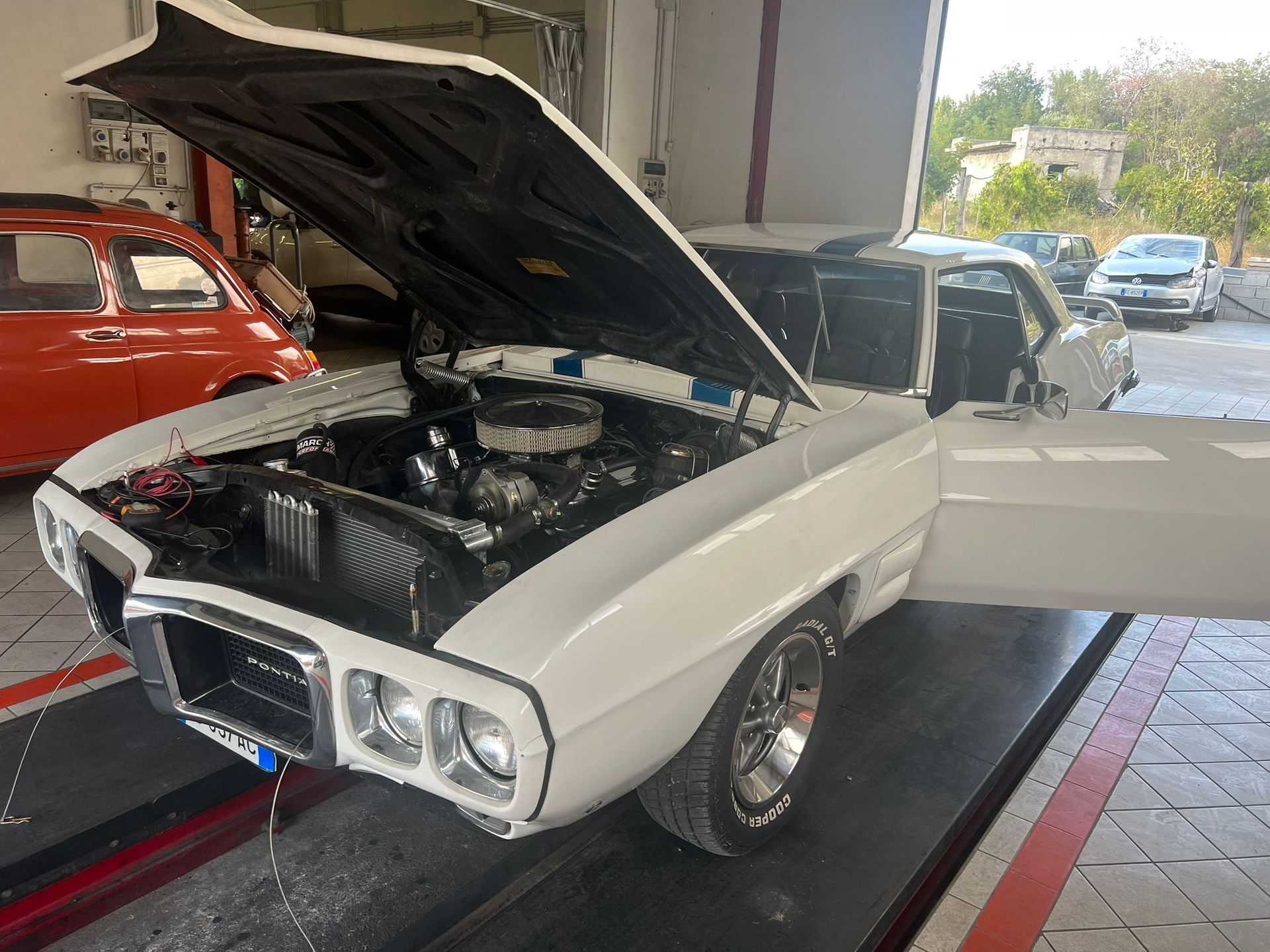 A white car with the hood up is parked in a garage.