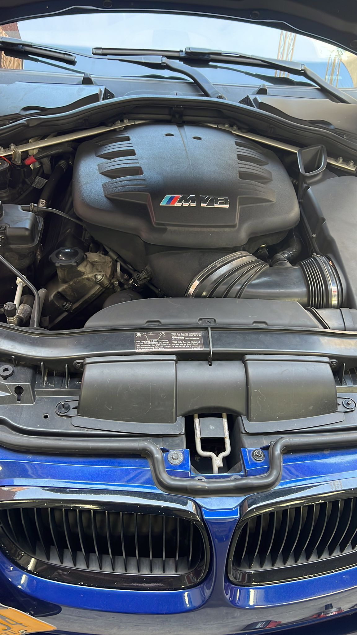 The engine of a blue bmw is shown with the hood open.