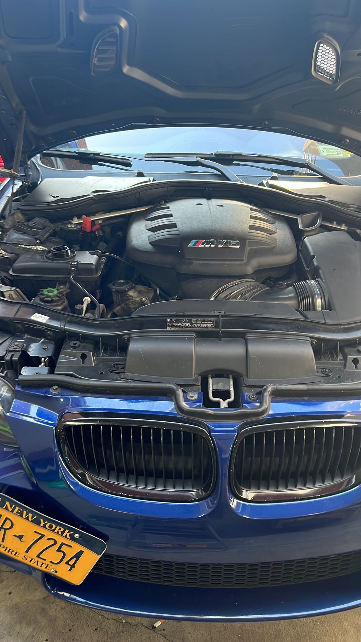 The hood of a blue bmw m3 is open and the engine is visible.