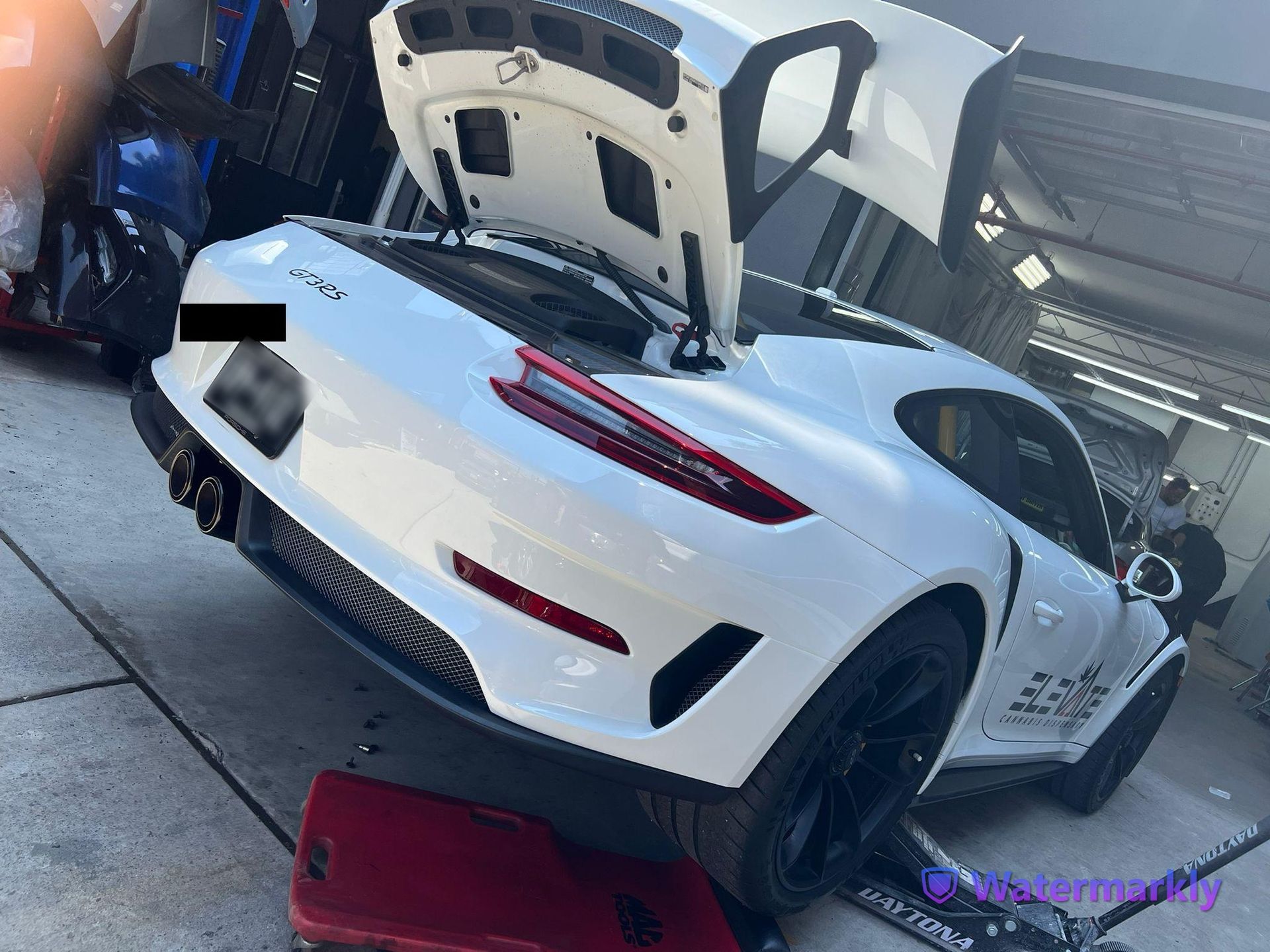 A white sports car with the hood up is parked in a garage.