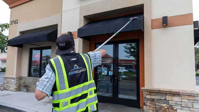 A man in a high visibility vest is cleaning the awning of a building.