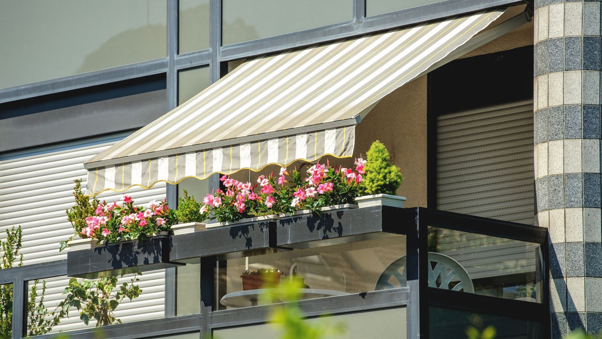 A balcony with flowers and a striped awning on it