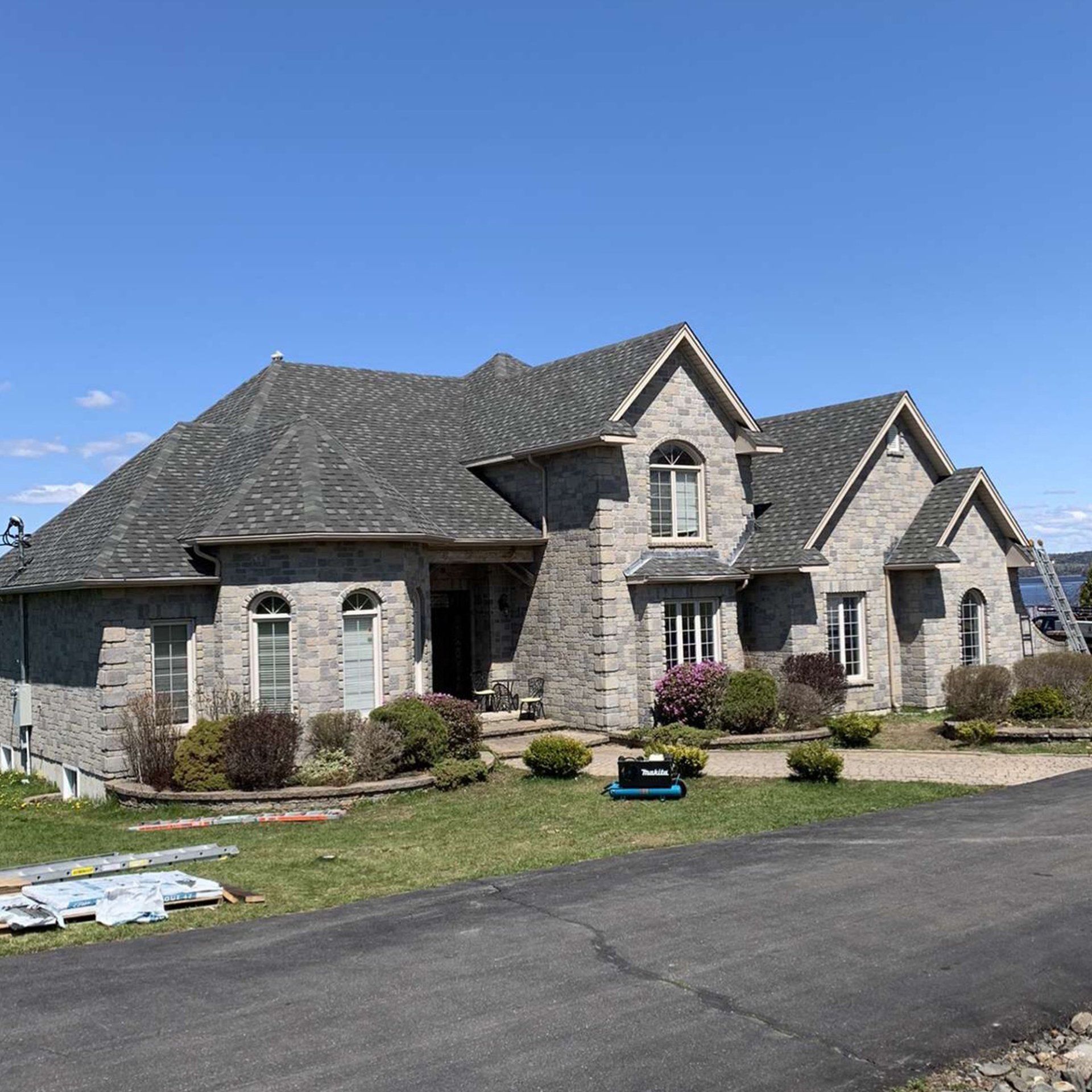 A large brick house with a gray roof is sitting next to a road.