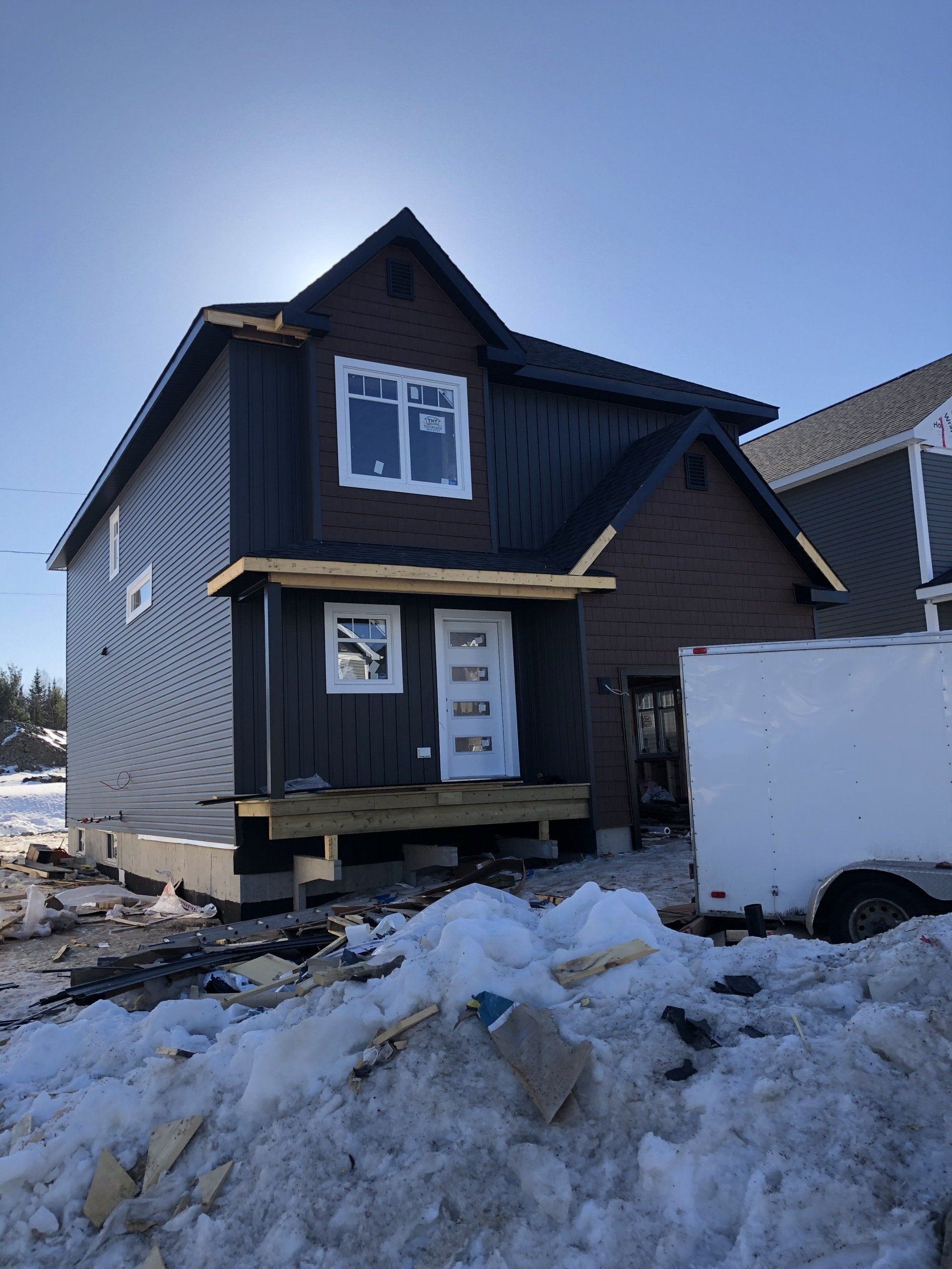 A house is being built in the snow next to a white truck.